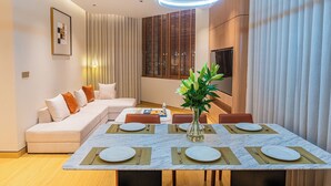 Un espace repas moderne avec une table en marbre dressée pour quatre personnes, un canapé avec des coussins et un vase rempli de fleurs.