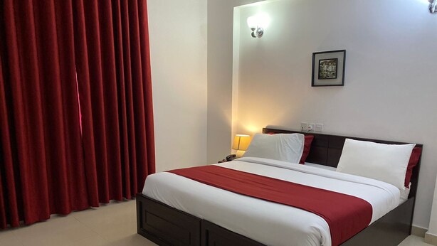 A neatly made bed with a red and white bedspread, a dark headboard, and a wall-mounted light fixture. - AZAIBA HOTEL APARTMENT (Muscat)