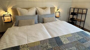 Ein ordentlich bezogenes Bett mit einem Patchwork-Quilt, zwei Nachttischlampen und einem Stadtbild darüber.