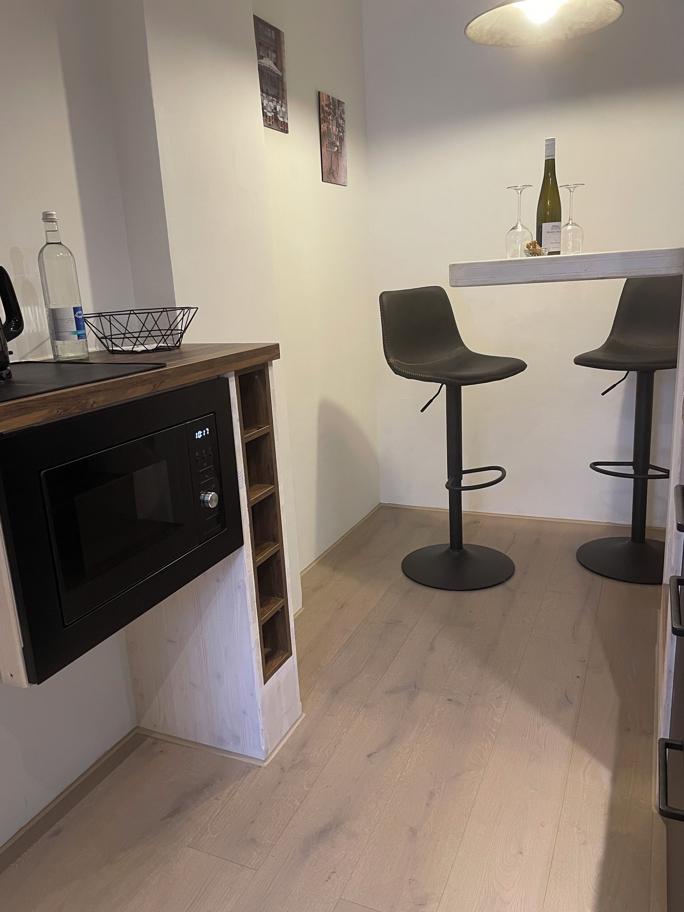 A kitchen with a built-in microwave, a wooden countertop, and two black bar stools.