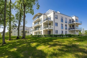 Un immeuble résidentiel à plusieurs étages, doté de balcons, d’une pelouse bien entretenue et surplombant un ciel bleu dégagé.