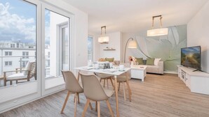Een moderne woonkamer met een eethoek, grote ramen en een flatscreen televisie.