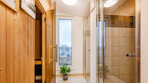 Een gang met houten wanden, een potplant, een douchecabine van glas en een deur naar een balkon met uitzicht.