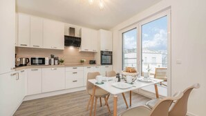Een moderne keuken met witte kastjes, een magnetron en een fornuis. Er is een eethoek met een tafel en stoelen.