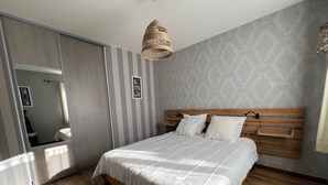 Une chambre à coucher avec un grand lit, une tête de lit en bois, un papier peint à rayures et un luminaire suspendu.