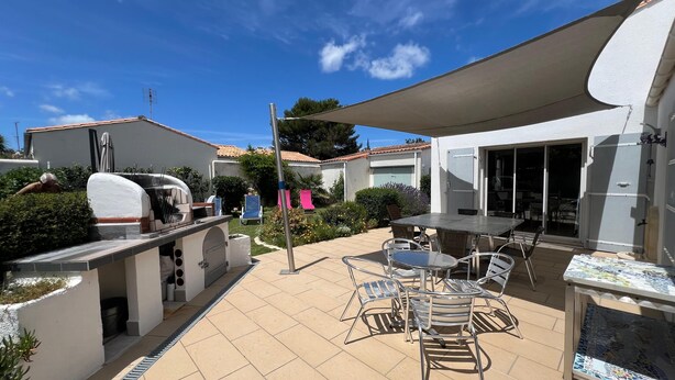 Un espace extérieur aménagé en patio, avec un barbecue, une table couverte et des chaises.