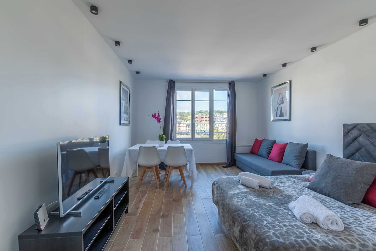 Une chambre d’hôtel moderne équipée d’un lit, d’un canapé, d’une table à manger avec des chaises, d’une télévision et d’une fenêtre avec des rideaux.