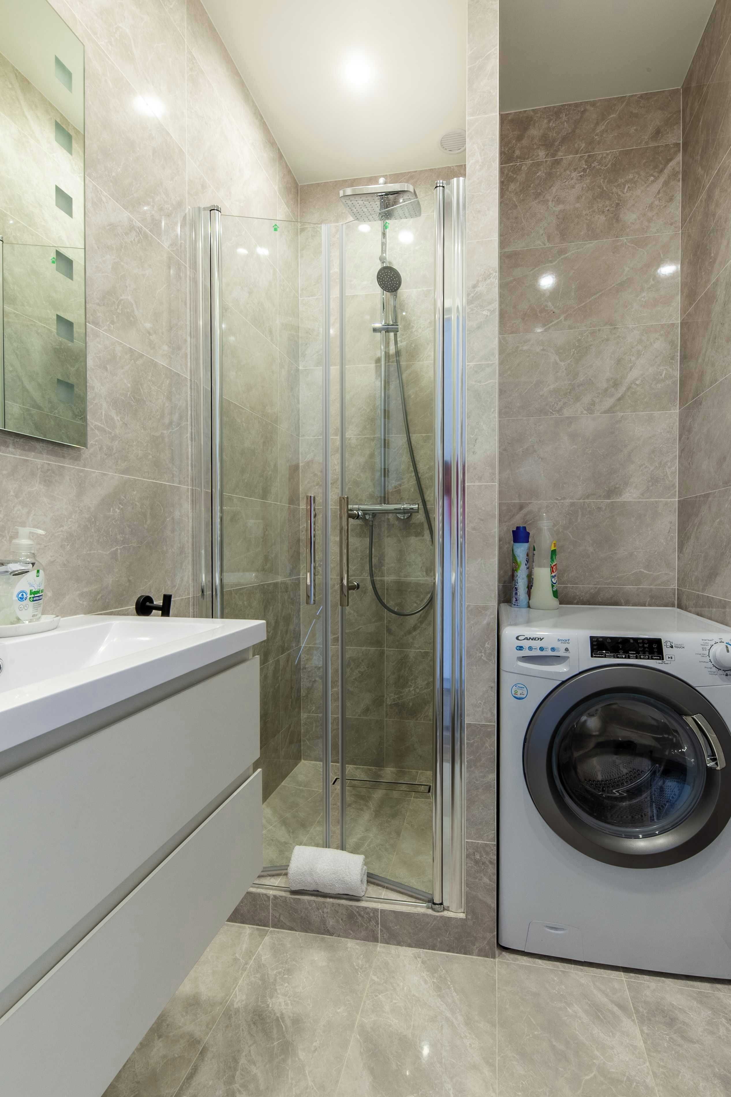 A modern bathroom with a glass-enclosed shower, a built-in washing machine, and a large mirror.