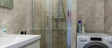 A modern bathroom with a glass-enclosed shower, a built-in washing machine, and a large mirror.