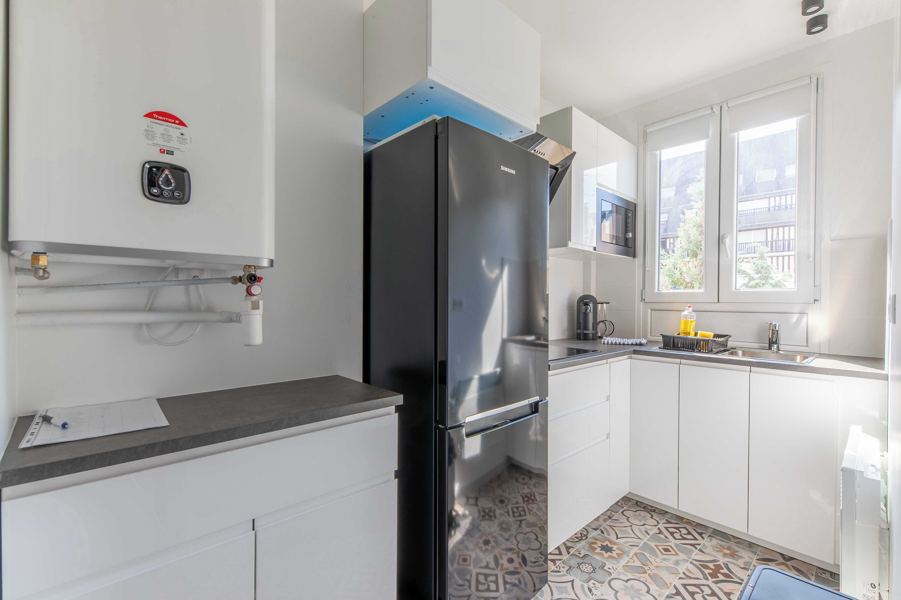 Una cocina moderna con armarios blancos, un refrigerador negro, un ventanal con vistas y piso de baldosas.