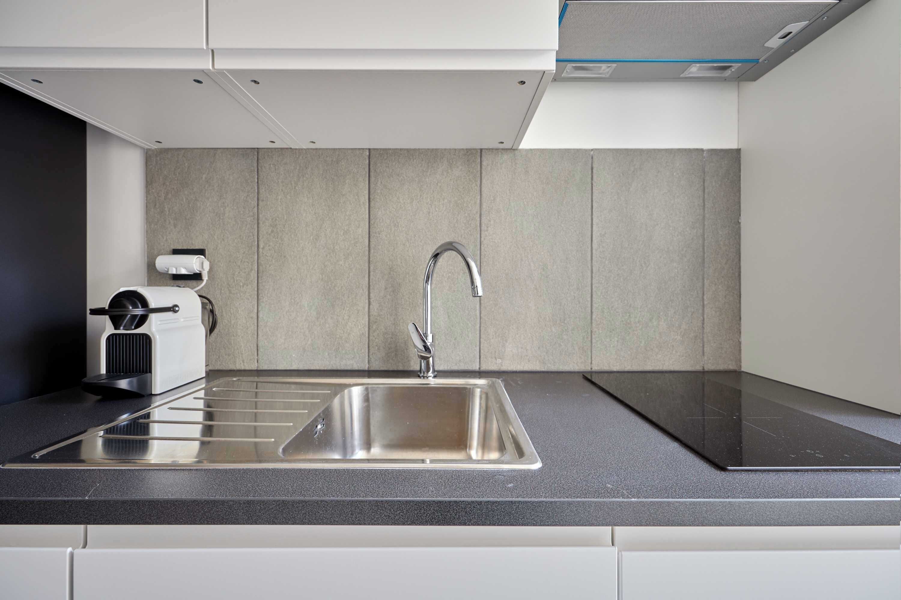 Una cocina moderna con un lavamanos de acero inoxidable, horno empotrado y una cafetera compacta.