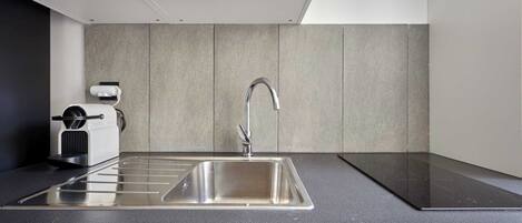 Una cocina moderna con un lavamanos de acero inoxidable, horno empotrado y una cafetera compacta.