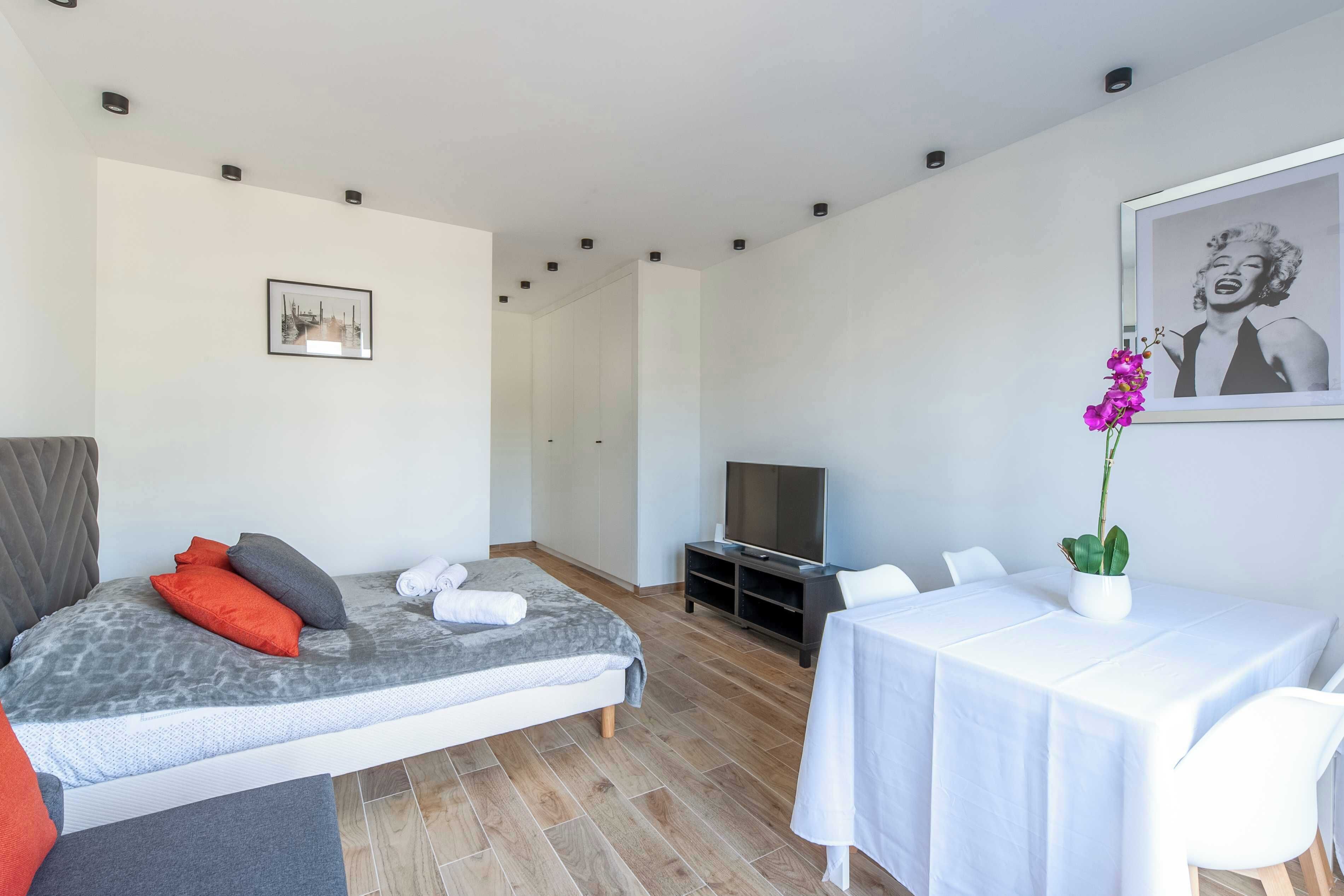 Habitación de hotel moderna con una cama, un televisor, una mesa de comedor y un cuadro en la pared.