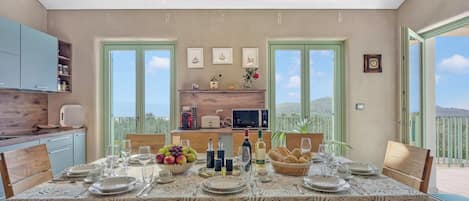 A dining area with a table set for four, kitchen cabinets, a window, and a balcony view.