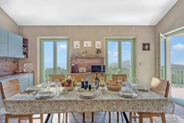 A dining area with a table set for four, kitchen cabinets, a window, and a balcony view. - Villa Olivia with Sauna (Piran)