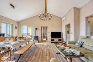 A spacious living room with a dining area, a fireplace, a television, and a sofa. - Villa Olivia with Sauna (Piran)