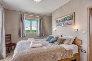 A bedroom with a bed, pillows, a window with curtains, a chair, and a painting on the wall. - Villa Olivia with Sauna (Piran)