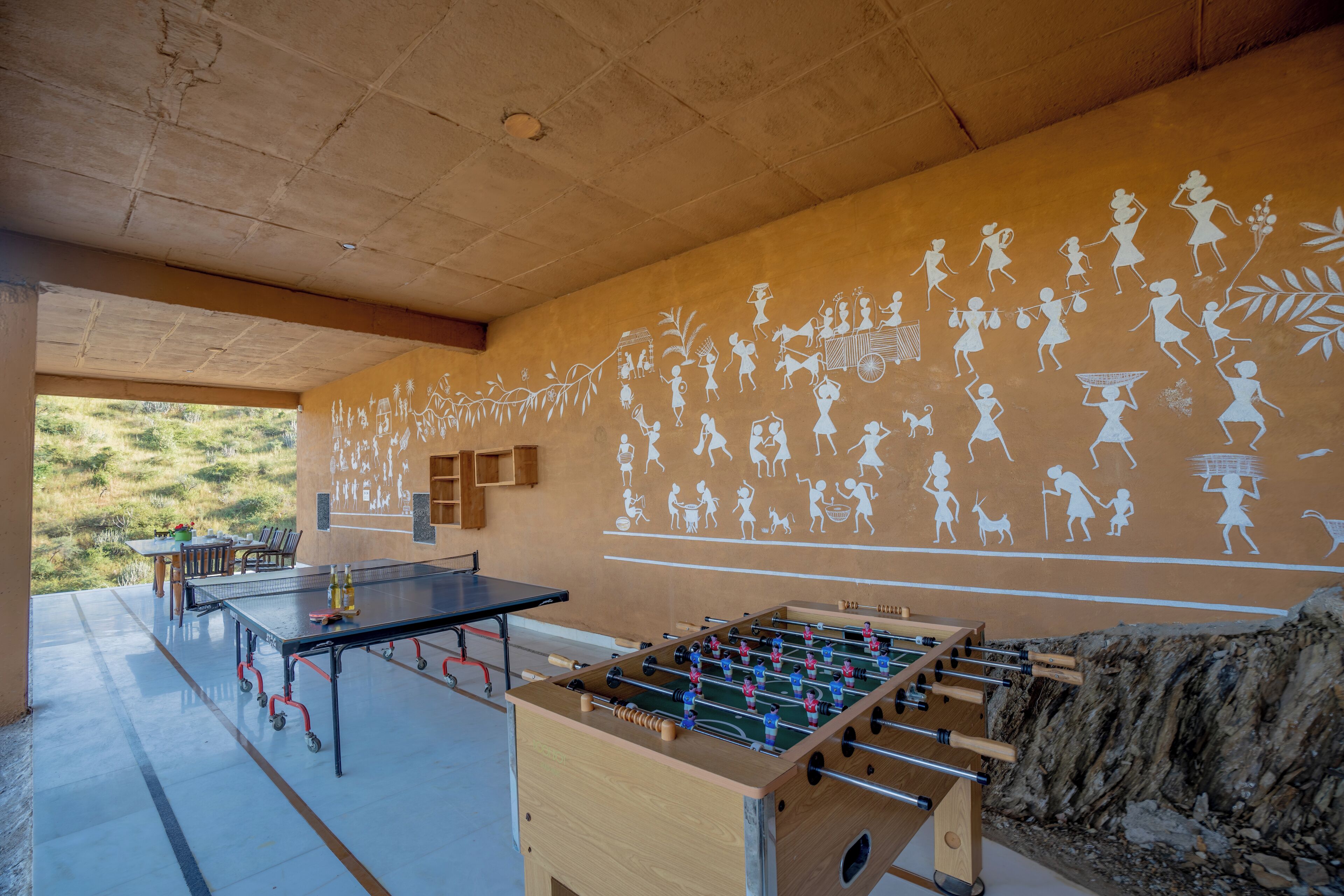 Quarto com mesa de futebol de mesa, mesa de ping pong e um mural retratando diversas atividades.