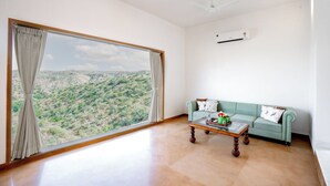 A spacious room with a large window offering a view of a hilly landscape, a light green sofa, and a wooden coffee table. - YAAN Estates (Khamnor)
