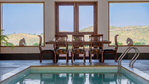 A pool area with a table and chairs, a view of hills, and a cat on the windowsill. - YAAN Estates (Khamnor)