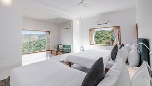 A modern hotel room with two beds, a green sofa, a dining table, and a large window offering a scenic view. - YAAN Estates (Khamnor)