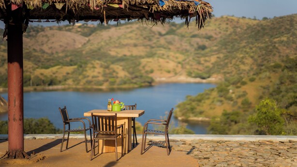 A table with chairs under a thatched roof, overlooking a lake and hilly landscape. - YAAN Estates (Khamnor)