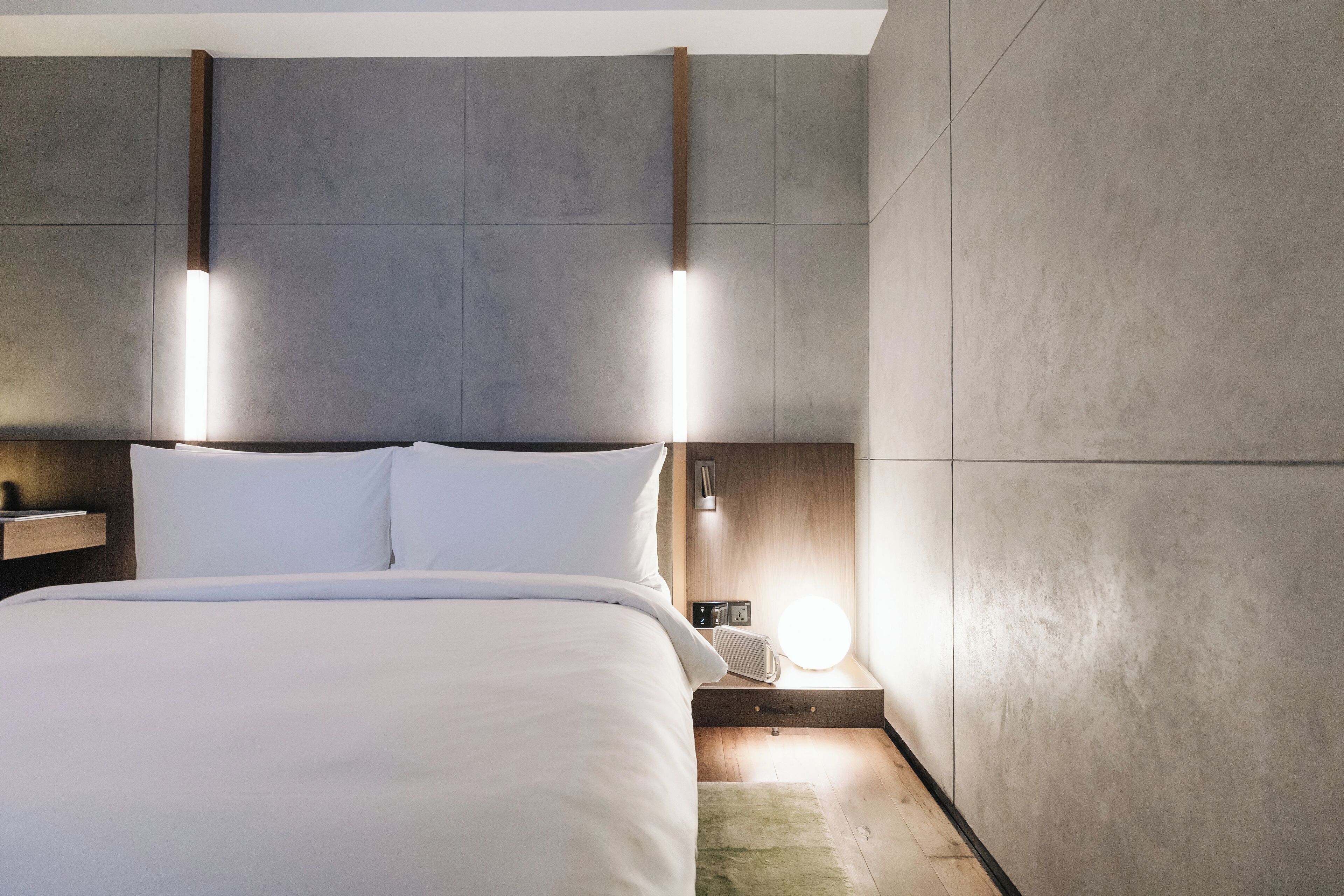 Una habitación de hotel moderna con una cama grande, una mesita de noche y una lámpara fijada a la pared.