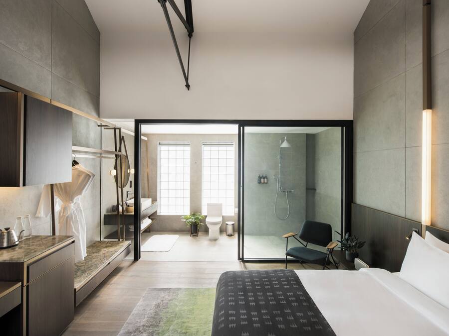 Habitación de hotel moderna con una cama grande, un vestidor, zona de ducha con mampara de vidrio y vistas al exterior.