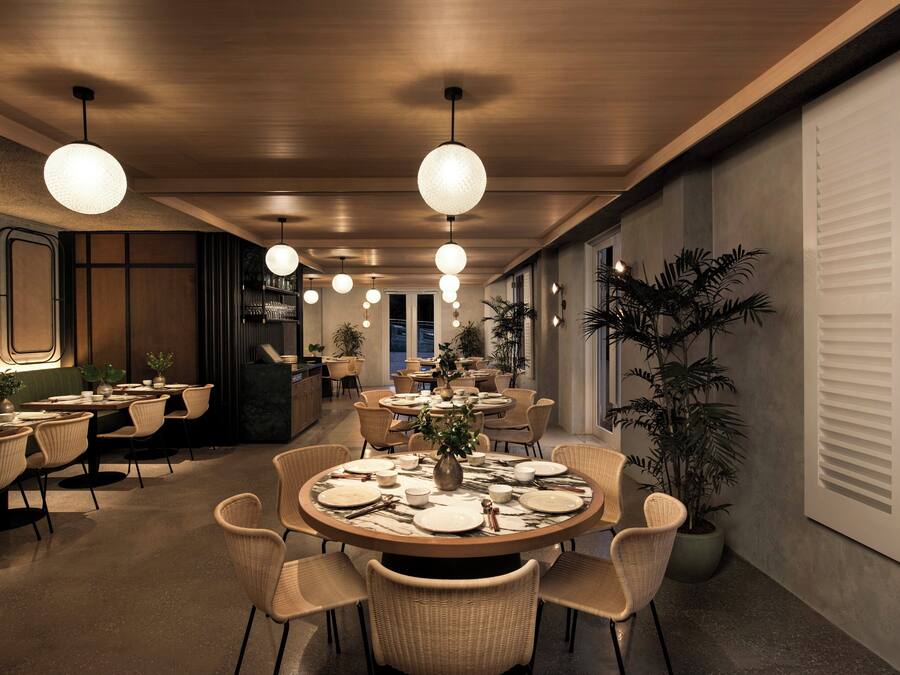 Un comedor moderno con mesas redondas, sillas de mimbre e iluminación colgante.
