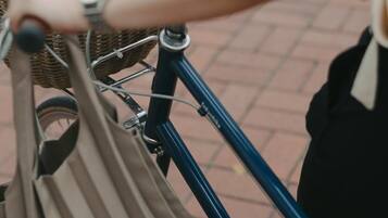 A close-up of a bicycle with a basket and a bag attached to the handlebars.