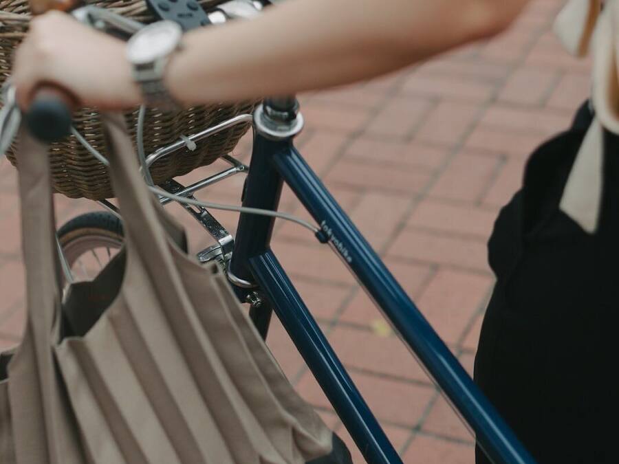 A close-up of a bicycle with a basket and a bag attached to the handlebars.
