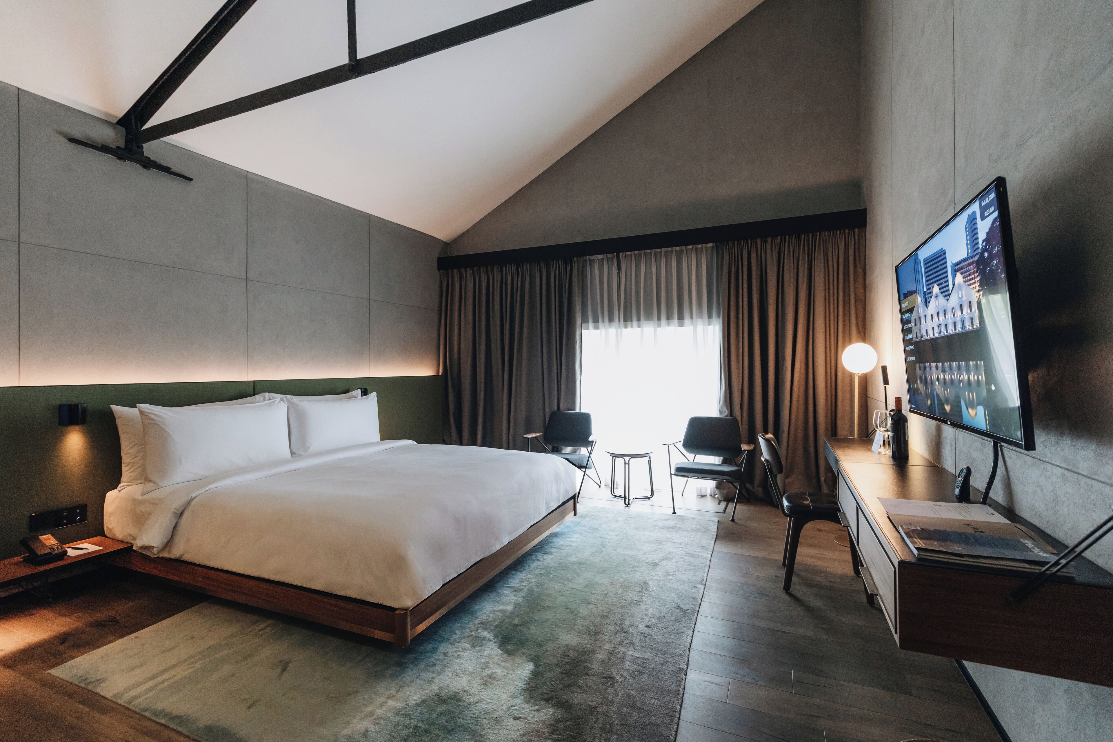 Une chambre d’hôtel moderne dotée d’un grand lit, d’un bureau, d’une télévision à écran plat et d’une fenêtre avec des rideaux.