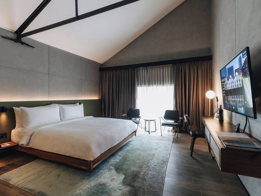 Une chambre d’hôtel moderne dotée d’un grand lit, d’un bureau, d’une télévision à écran plat et d’une fenêtre avec des rideaux.