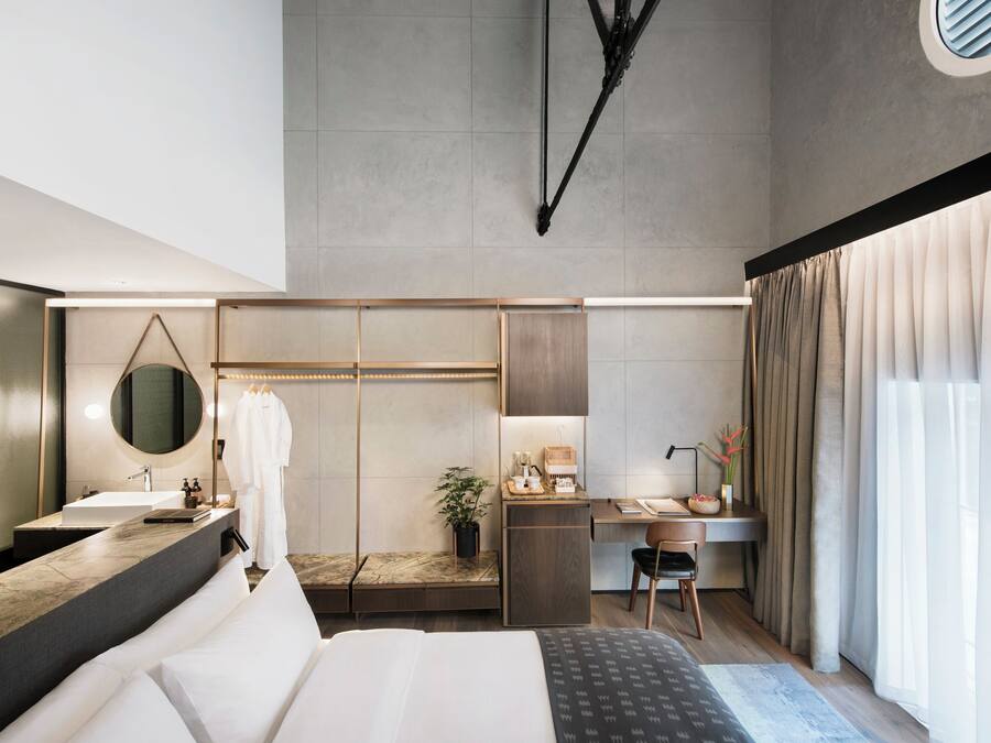 Una habitación de hotel moderna con una cama grande, un escritorio, una tocador con espejo y un ventanal con cortinas.