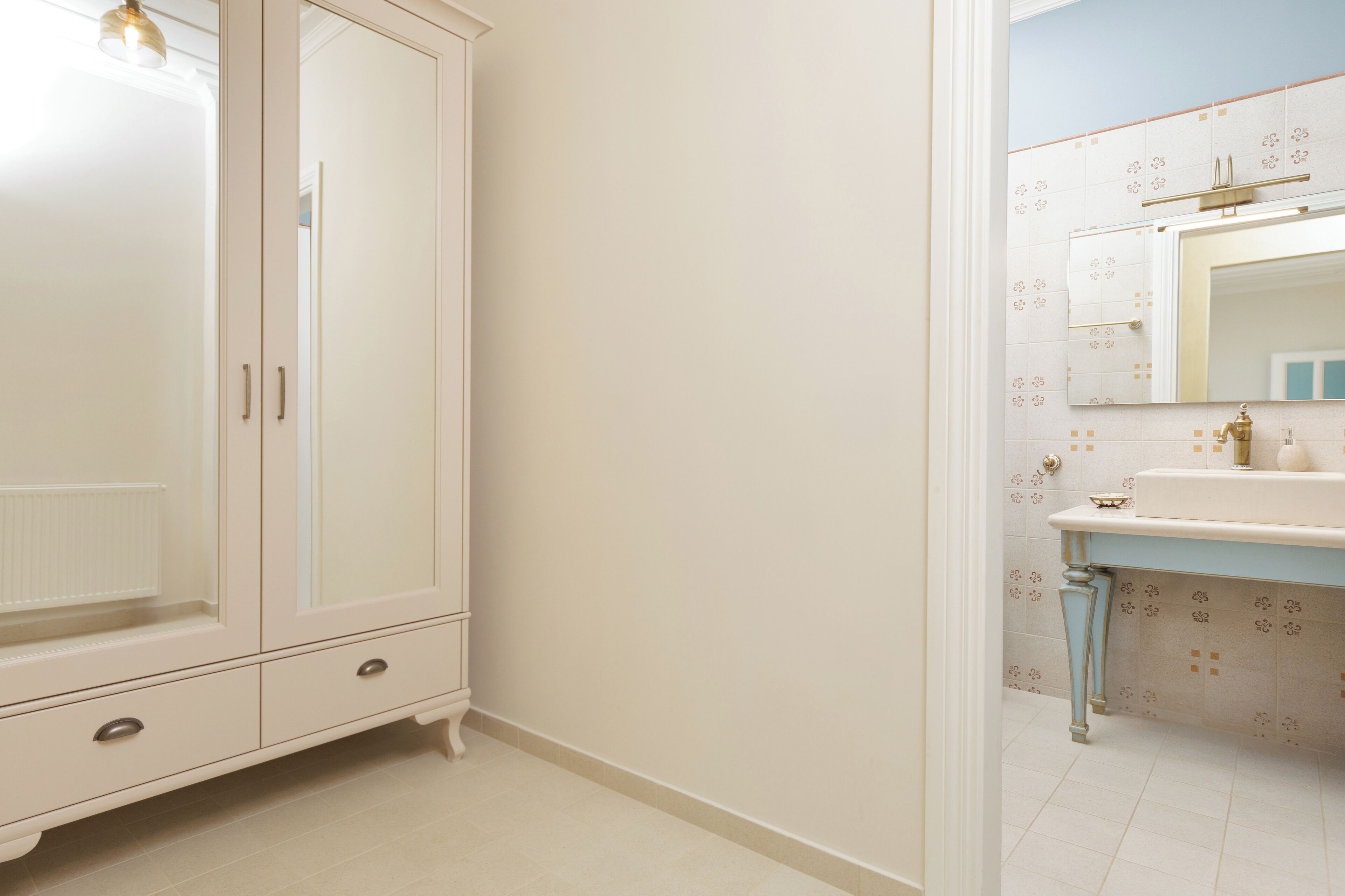Une salle de bain avec un placard blanc, un lavabo avec un miroir et des carreaux décoratifs sur les murs.