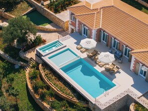 A large rectangular swimming pool with two smaller pools, surrounded by stone walls and lush greenery. - Archontiko Stoufi, an Authentic SeaView Retreat (VMHW+8F Skinaria, Greece)