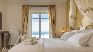 Een hotelkamer met een groot bed, uitzicht op zee door een raam, en een hemelbed.