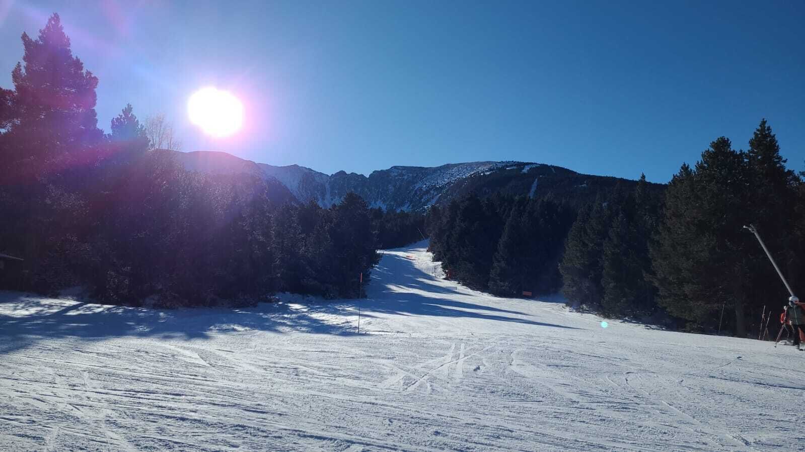 A snowy ski slope with trees and mountains in the background.