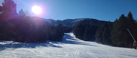 A snowy ski slope with trees and mountains in the background.