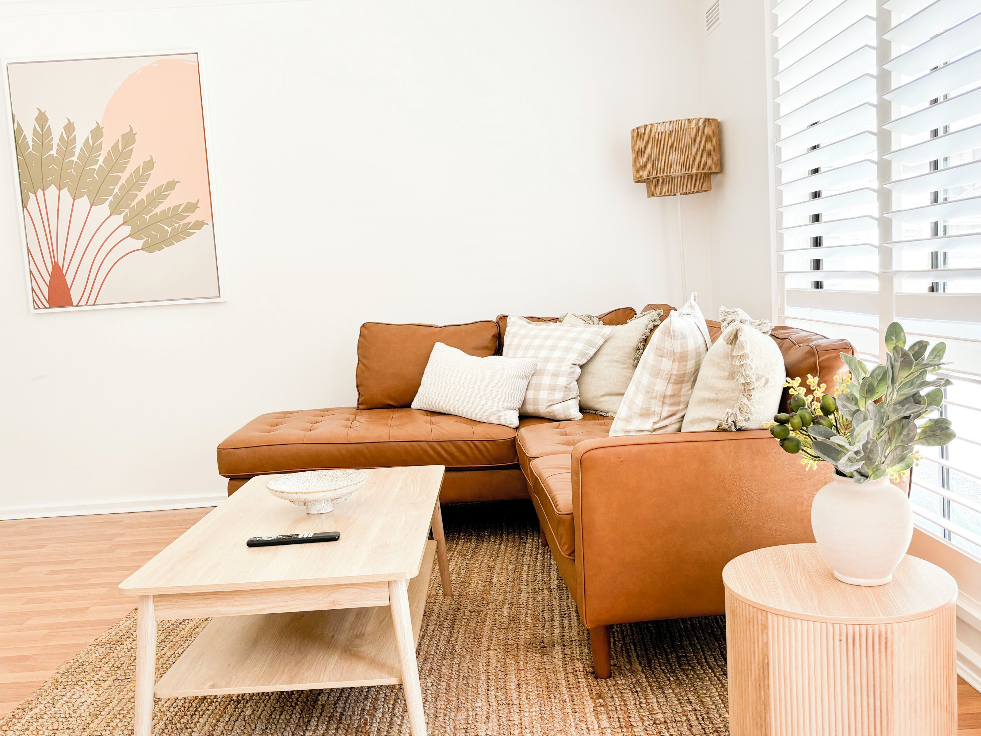 A modern living room with a brown leather sofa, a wooden coffee table, and a small round side table with a vase.