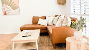 Una sala de estar moderna con un sofá de cuero marrón, una mesa de centro de madera y una mesita auxiliar redonda con un florero.