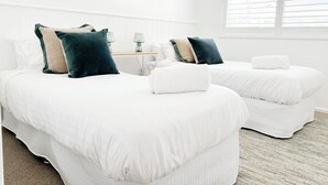 Una habitación de hotel con dos camas, ropa de cama blanca y una mesita con lámpara.