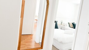 A bedroom with a wooden-framed mirror, a bed with white bedding, and a nightstand with a lamp. - Haven in the heart of Turvey Park! (Wagga Wagga)
