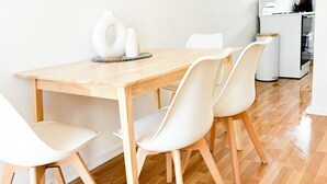 Un comedor con una mesa de madera y sillas blancas, una cocina al fondo y una pared blanca.