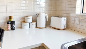 Une cuisine avec des murs recouverts de carreaux blancs, un plan de travail blanc, un grille-pain, une bouilloire et des récipients de rangement.