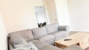 Un salon avec un canapé gris, une table basse en bois et une télécommande posée dessus.