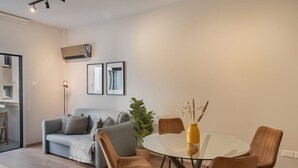 Ein modernes Wohnzimmer mit einem Glastisch, braunen Stühlen, einem grauen Sofa und einer Topfpflanze.