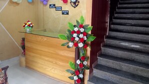 A reception desk with a glass top, surrounded by a wooden panel wall. There are signs indicating rental car and booking services, and a clock on the wall. - Nest Hotel (Rawalpindi)