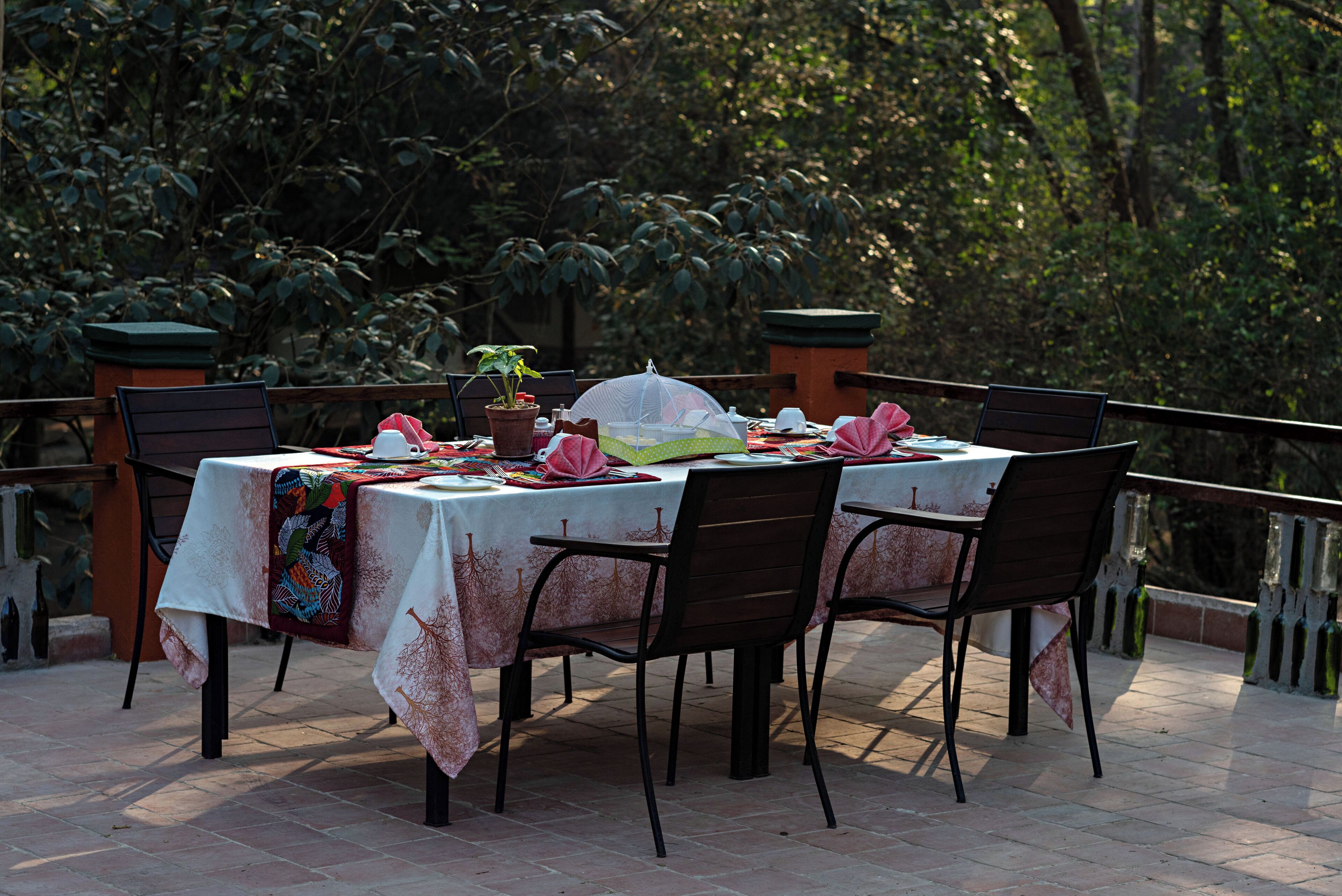 An outdoor dining area with a table set for four, surrounded by chairs, and a potted plant on the table.