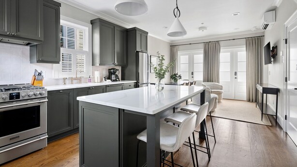 A modern kitchen with a central island, stainless steel appliances, and a dining area with bar stools. - Thomas Waring House | Unit D | Sleeps 6 (Charleston)